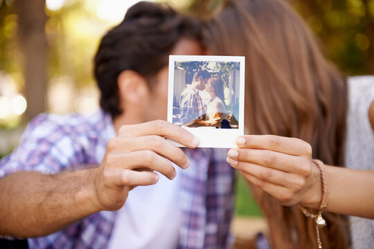 Couple, photograph and valentines day date with love, kiss and affection in outdoor park for memory. Happy man and woman together on a picnic with polaroid paper picture in hands on holiday outdoor