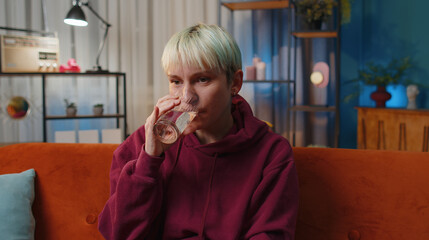 Thirsty woman with short blonde hair holding glass of natural aqua make sips drinking still water...