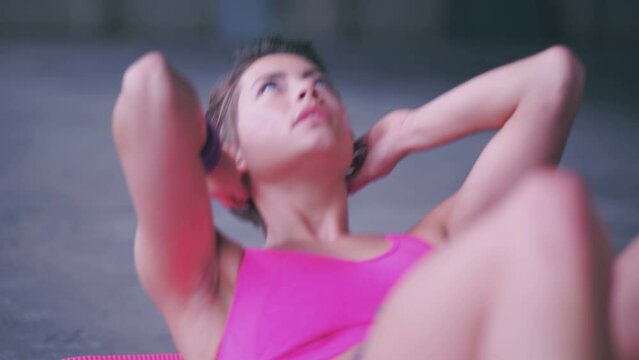 Serious teenage girl on a pink exercise mat doing stomach crunches and sit ups