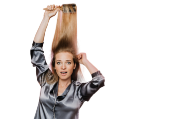 Shocked redhead young woman wearing pyjama, brushing her hair with scared face, posing over transparent background with copy space. Woman's morning preparing she is late for work.
