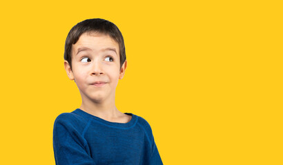 Dark haired little child with blue shirt over isolated yellow background looking away to side with...