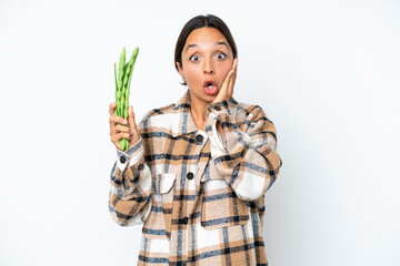 Young hispanic woman holding a green beans isolated on white background with surprise and shocked facial expression