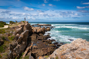 A man standing alone on rocky cliffs along the Cliff Path looking out to Walker Bay and the ocean...