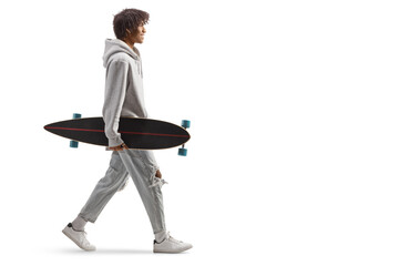 Full length profile shot of an african american guy carrying a longboard and walking