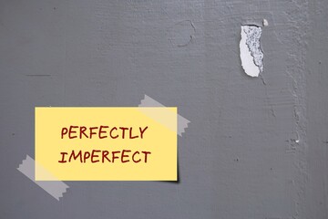 Yellow note on gray wall with handwritten text PERFECTLY IMPERFECT, concept of accept yourself no...