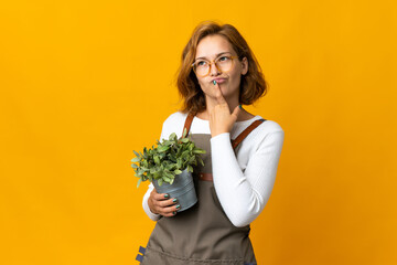 Young Georgian woman holding a plant isolated on yellow background having doubts while looking up