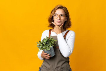 Young Georgian woman holding a plant isolated on yellow background having doubts