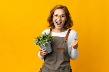 Young Georgian woman holding a plant isolated on yellow background celebrating a victory in winner position