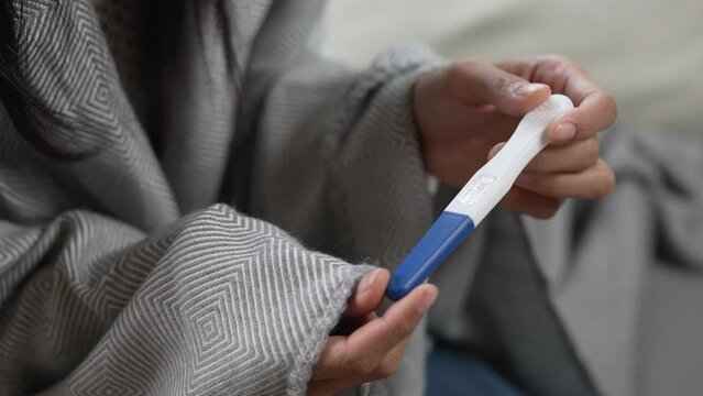 Depressed young Asian woman feeling sad while looking at the positive results of a pregnancy test.
