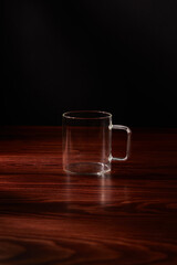 empty glass cup stands on a wooden table on a black background