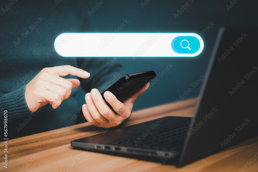 Poster Adult man hand working with a mobile phone and computer laptop on the desk. Searching browsing internet data information with blank search bar. Search Engine Optimization SEO networking concept.