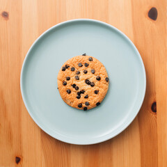 Chocolate chip cookie on light blue plate, on wooden surface, flat lay