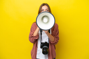 Young photographer caucasian woman isolated on yellow background shouting through a megaphone