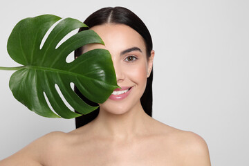 Woman holding leaf of monstera on light grey background. Spa treatment