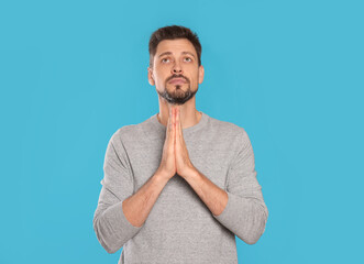 Man with clasped hands praying on turquoise background