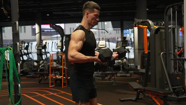 Athletic man making biceps triceps curls workout in fitness gym. Athlete exercising with dumbbells