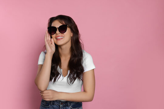 Happy beautiful woman with stylish sunglasses on pink background, space for text