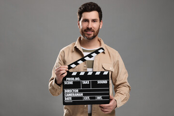 Smiling actor holding clapperboard on grey background