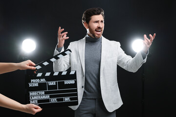 Emotional actor performing while second assistant camera holding clapperboard on black background - obrazy, fototapety, plakaty
