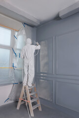 Decorator dyeing wall in grey color with spray paint indoors