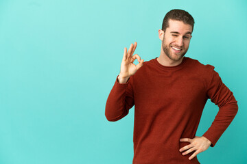 Handsome blonde man over isolated blue background showing ok sign with fingers