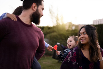 The interracial family is active and enjoys a day at the park. Successful adoption. Parents carry children on their backs while they bump lollipops. Concept of multiethnic-interracial family.
