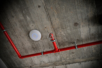 A detail of a rustic ceiling with red pipes and a fire alarm
