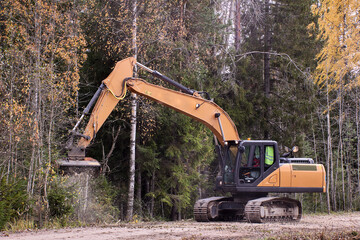 Forestry mulching machine attached to excavator, being used to clear roadside brush. © grigvovan