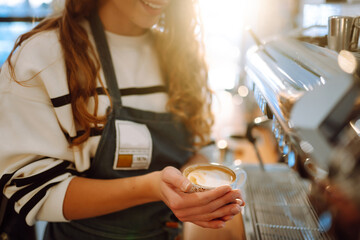 Barista  holds a cup with coffee in his hands. A drawing is drawn on coffee foam. Food and drink concept.