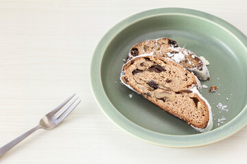 Sliced Stollen and fork on a round khaki plate on a white wooden table