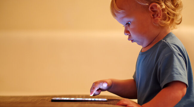 Small Baby Pressing And Scrolling With Finger On Phone Touch Screen. Cute Little Child Learns To Use New Internet Technologies. Baby Playing With Cellphone, At Home In The Evening.