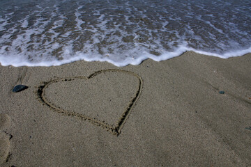 Heart on the beach. The sea wave washes away the heart drawn on the sand.