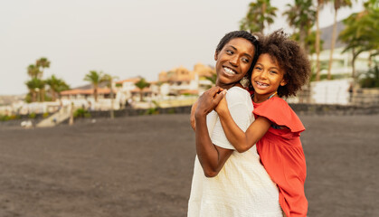 Fototapeta premium Happy African mother and daughter having fun on the beach during vacations - Lovely family lifestyle concept