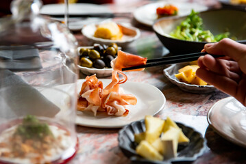 man hand eating prosciutto in restaurant. wine, cheese, meat, vegetables and other appetizers on table