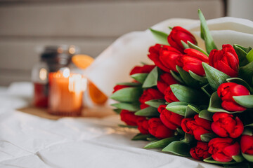 Bouquet of red tulips lying on bed by tea and burning candle