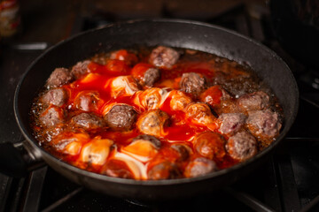 Cooking homemade meatballs in a frying pan in a sauce of tomatoes and sour cream.