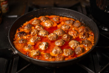 Cooking homemade meatballs in a frying pan in a sauce of tomatoes and sour cream.