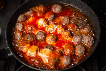 Cooking homemade meatballs in a frying pan in a sauce of tomatoes and sour cream.