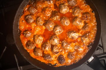 Cooking homemade meatballs in a frying pan in a sauce of tomatoes and sour cream.