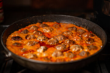 Cooking homemade meatballs in a frying pan in a sauce of tomatoes and sour cream.