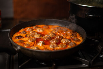 Cooking homemade meatballs in a frying pan in a sauce of tomatoes and sour cream.