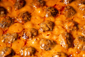 Cooking homemade meatballs in a frying pan in a sauce of tomatoes and sour cream. Close-up macro. Food background.