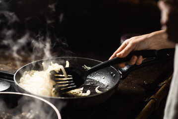 onions are fried in a pan and steam comes from cooking. Roasting onions.