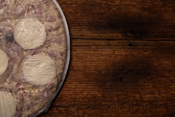 Frozen pizza on a wooden background. Semi-finished pizza packed in film.