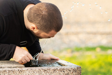 drinking fountain, a man drinks water from a fountain in a park on a sunny day