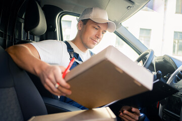 The driver is a male courier company in the car. A courier employee delivering boxes by car to the...