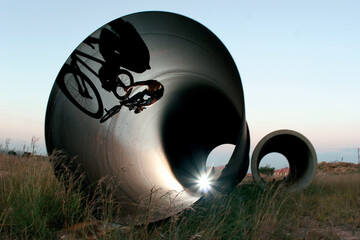 A BMX rider silhouetted as he rides inside a huge metal pipe.