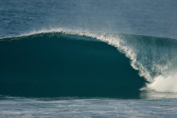 A perfect blue wave breaks in the ocean.	