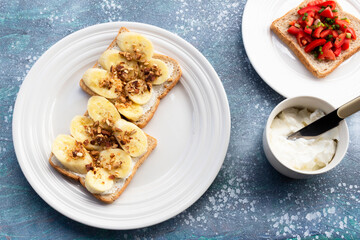 Sandwich breakfast has banana cream cheese almonds and tomato on blue wood table.