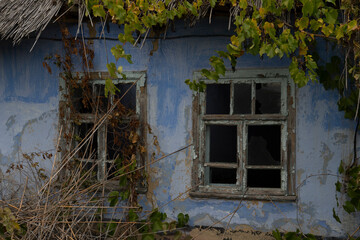 Old crumbling house with two windows without glass, reed roof
